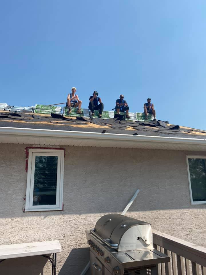 Four roofers working together on a residential roof installation under clear skies in Regina.